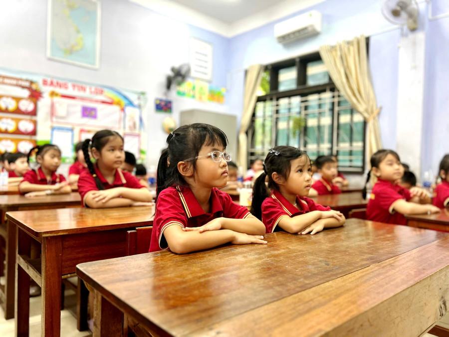 Học sinh ngồi ngay ngắn trong lớp học, đôi mắt mở to, tò mò trước bảng đen và phấn trắng. 9.jpg