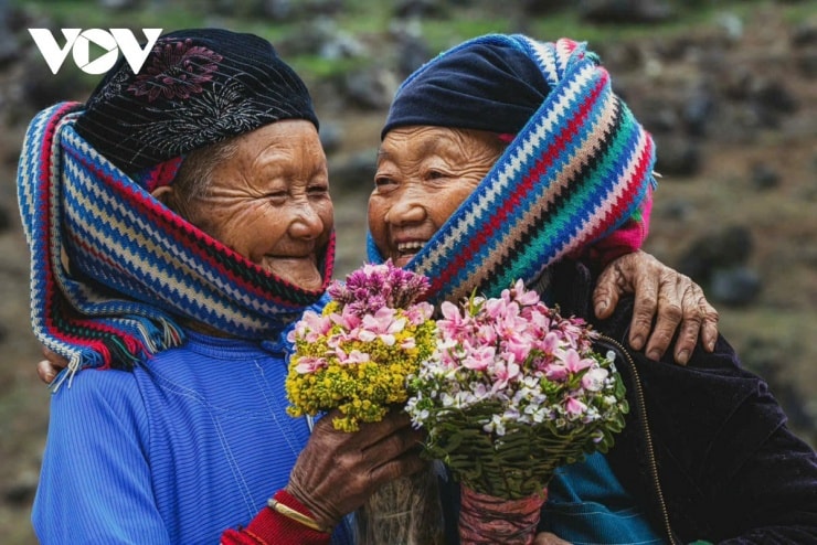 Cụ bà người Lô Lô trong trang phục truyền thống ngồi bên hiên nhà.